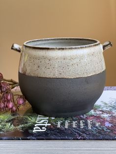 a gray and white bowl sitting on top of a book next to flowers in a vase