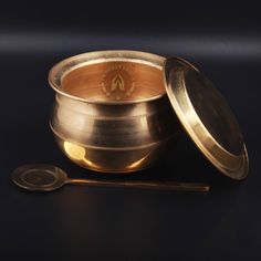 an antique brass bowl and spoon on a black surface with the lid open to show it's contents