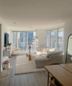 a living room filled with furniture and large windows next to a wooden floor covered in white rugs