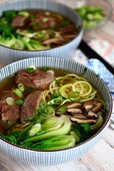 two bowls filled with soup and vegetables on top of a wooden table