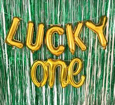 the words lucky one are spelled out in gold foil balloon letters on a green background