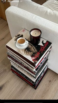 a stack of books sitting on top of a white couch next to a cup of coffee