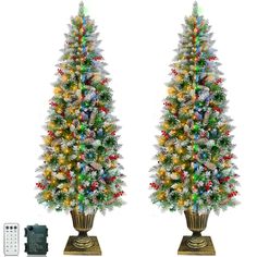 two artificial christmas trees with lights and ornaments on stands next to a remote control controller