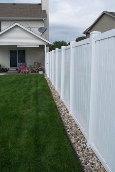 a white picket fence in front of a house with grass and rocks on the ground