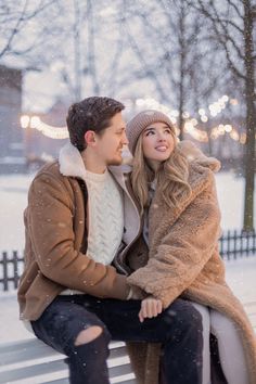 a young man and woman sitting on a bench in the snow looking into each other's eyes