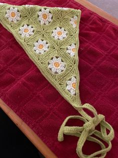 a crocheted triangle on top of a red blanket with white and yellow flowers