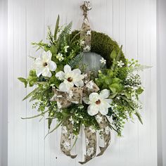 a wreath with white flowers and greenery hanging on a wall