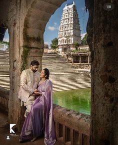 a man and woman standing next to each other in front of a building with water