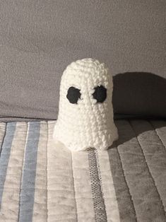 a crocheted ghost hat sitting on top of a bed next to a pillow