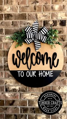 a welcome sign hanging on the side of a brick wall with a black and white bow