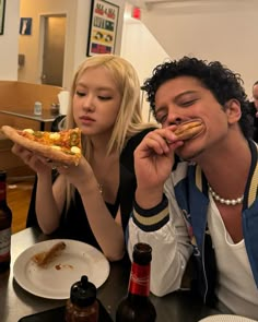 two people sitting at a table eating pizza and drinking beer, one woman is holding a slice of pizza in front of her face