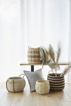 several woven baskets and pillows on a wooden floor in front of a window with white curtains