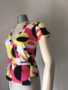 "90s Vintage does 70s stretchy double breasted top that features a very cool, geometric squared and circles pattern Shocking pink and bright yellow mixed with black and white makes it so groovy and some may say rave? It ties with a long cord all around the waist. It was then, in the early 90s that the super stylish dance band \"Deee Lite\" brought back that psychedelic style in fashion. (All the credits to the band!) ‼️Be aware - only one piece is available----- 🌀MEASUREMENTS: (taken while layi Retro V-neck Stretch Top, Fitted Abstract Print Summer Tops, Trendy Fitted Top With Abstract Print, Fitted Summer Tops With Retro Print, Yellow Retro Print Top For Summer, Bold Graphic Print Tops For Spring, Fitted Black Top With Geometric Pattern, Bold Multicolor Summer Tops, Colorful Summer Top With Yellow Pattern