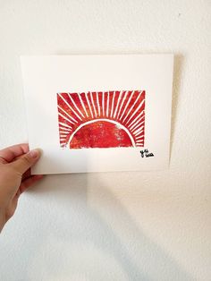 a hand holding up a red and white card with an image of the sun on it