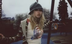 a woman standing in front of a playground with her hands on the bars and wearing a hat