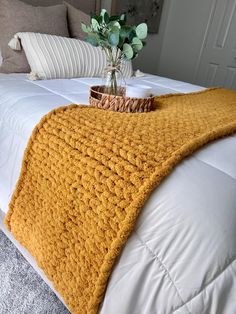 a crocheted blanket on top of a white bed with pillows and a vase filled with flowers