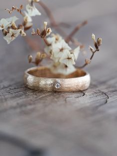 a close up of a wedding ring on a wooden surface with flowers in the background