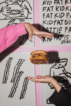 two people holding sandwiches in their hands while standing next to some drawings on the wall