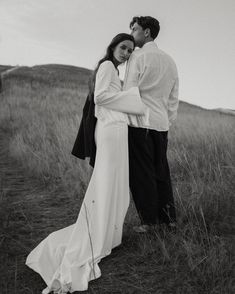 a man and woman standing next to each other in a field with tall grass on the ground