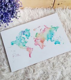 a watercolor map of the world on white paper next to purple and blue flowers