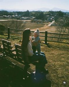 a woman sitting on top of a wooden bench next to a baby in her lap