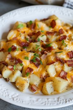 a white plate topped with potatoes covered in cheesy bacon and melted green onions