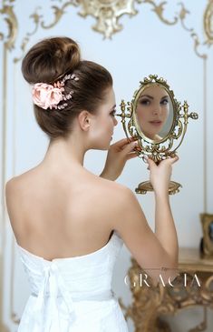 a woman in a white dress is looking at her reflection in a mirror with a flower in it