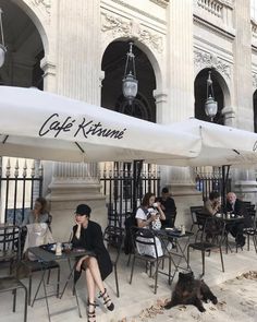 people sitting at tables under umbrellas in front of a building