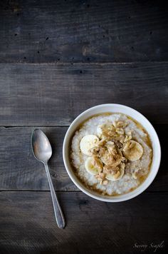 a bowl of oatmeal topped with bananas and nuts next to a spoon