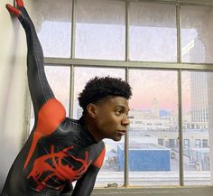 a woman in black and orange bodysuit leaning against a window