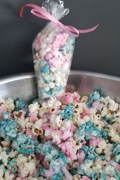 a bag of popcorn with pink and blue sprinkles in it sitting on top of a metal bowl