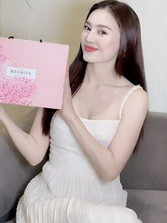 a woman sitting on a couch holding up a pink box with words written on it