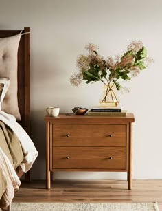 a bedroom with a bed, nightstand and flowers on the night stand next to it