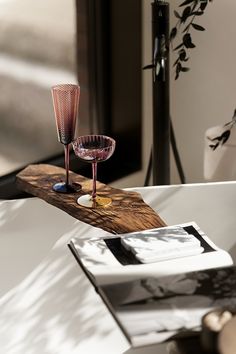 two wine glasses sitting on top of a wooden table next to a book and vase