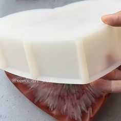 a hand holding a bar of soap on top of a flower shaped object with pink petals