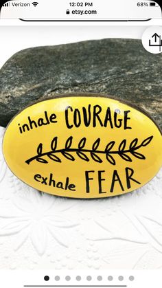 a yellow sign that says inhale courage exhale fear next to a rock