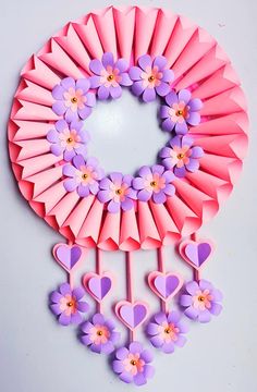 a pink paper wreath with purple flowers and hearts hanging from the front, on a white background