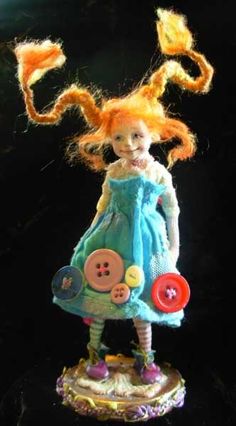 a doll with red hair wearing a blue dress and holding a button on her hand