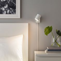 a bed with white sheets and pillows next to a green plant in a glass vase