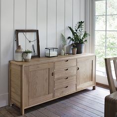 a wooden dresser sitting next to a window with potted plants on top of it