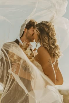 a bride and groom kissing under veils in the desert