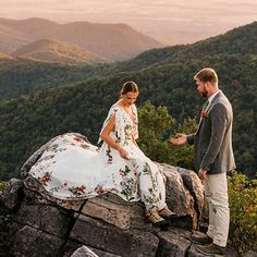 a bride and groom sitting on top of a rock in the mountains talking to each other