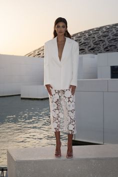 a woman standing on top of a cement block next to the ocean with her hands in her pockets