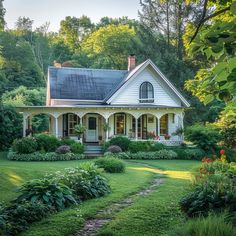 a white house surrounded by lush green trees and flowers in the front yard with a pathway leading to it