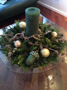 a candle is sitting on top of a glass plate with greenery and baubles