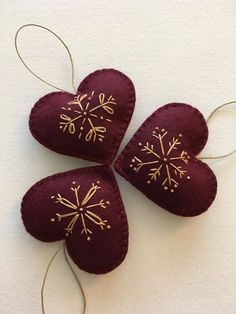 three red hearts with gold snowflakes are hanging on a white wall and one has two strings attached to it