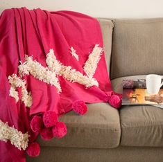 a coffee cup and magazine on a couch with a pink blanket draped over the sofa