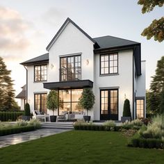 a large white house with lots of windows and plants on the front lawn, surrounded by greenery