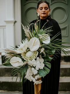 a woman standing in front of a green door holding a bouquet of white flowers and greenery