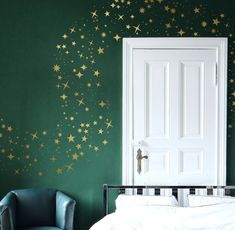 a green bedroom with gold stars painted on the wall and a white bed in front of it